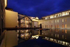 A hotel courtyard with a reflective pool, a building with large windows, and a well-lit facade. - Ruyi Resort · International Cultural Center of Buddhism, Putuoshan (Zhoushan)
