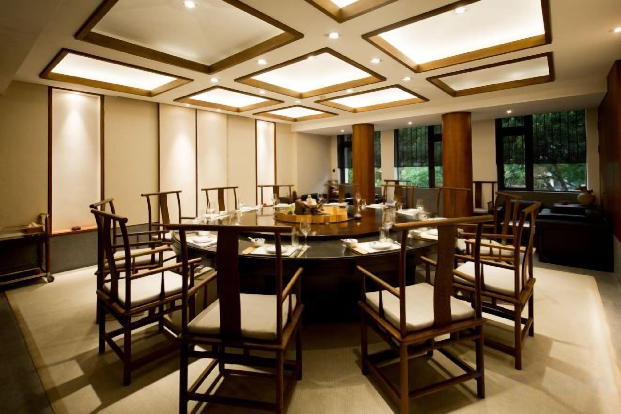 Un espace repas avec une table ronde entourée de chaises, un éclairage encastré au plafond et de grandes fenêtres.