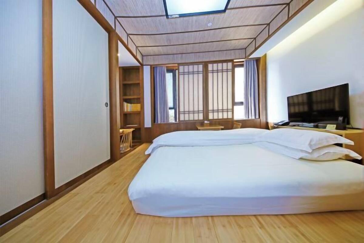 A hotel room with a bed, a TV, a desk, and a window with blinds.