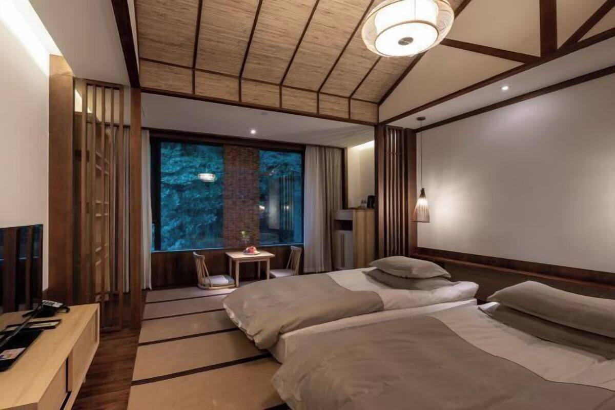 A modern hotel room with a large bed, a desk, and a window with a view of trees.