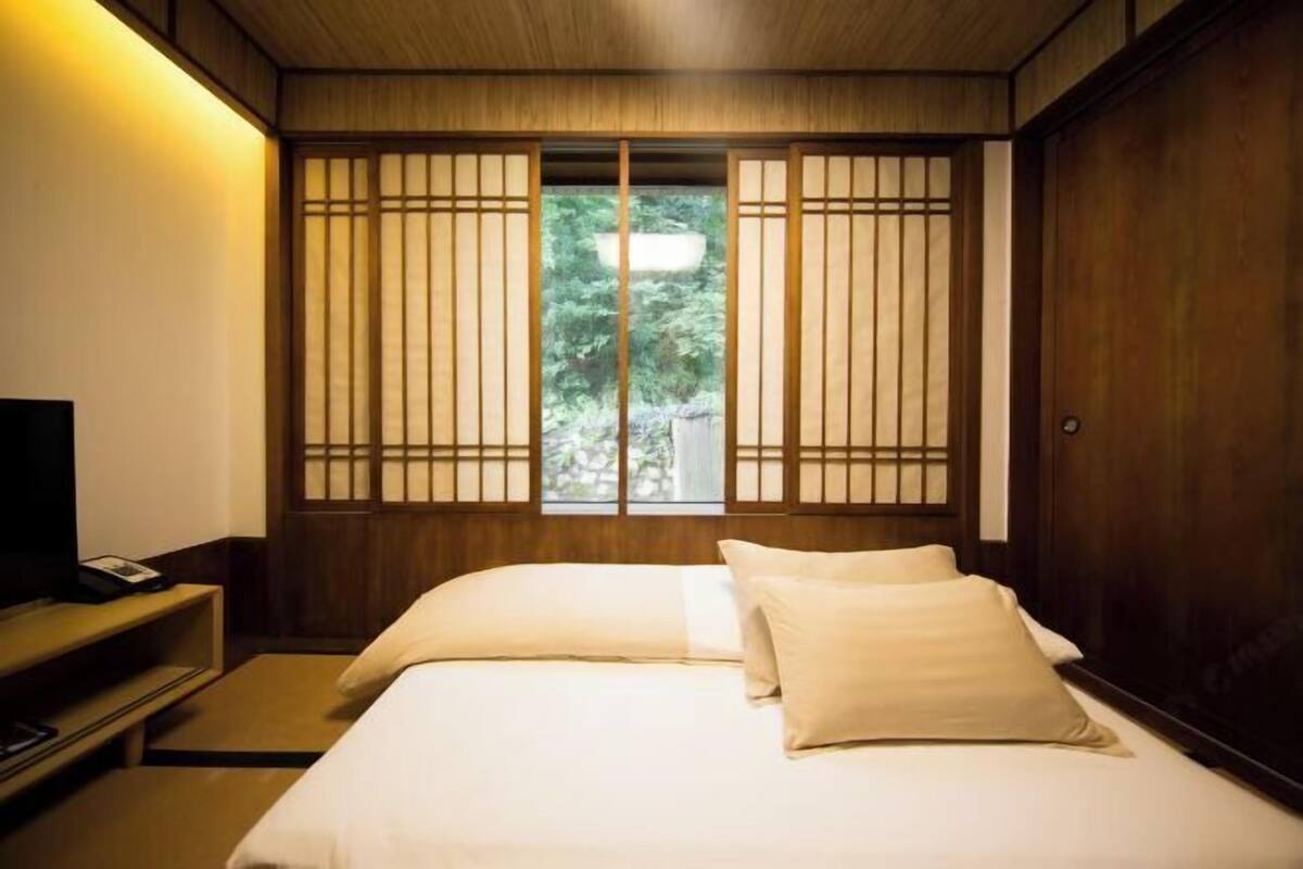 A hotel room with a bed, a TV, and a window with a view of greenery.