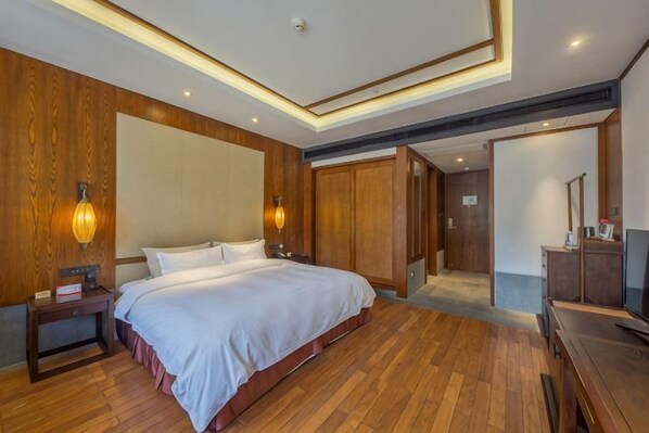 Habitación de hotel con una cama grande, suelo de madera, un escritorio con una silla, televisión y armario.