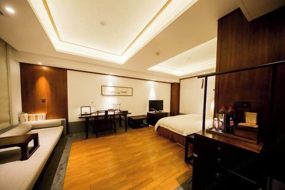 A hotel room with a bed, a desk, a sofa, a TV, and a wooden wardrobe.