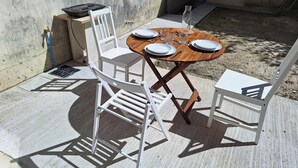 Une terrasse extérieure avec une table en bois, dressée pour quatre personnes, entourée de chaises blanches.