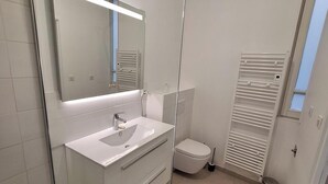 Une salle de bain moderne avec un meuble-lavabo blanc, un miroir, des toilettes et un espace douche.