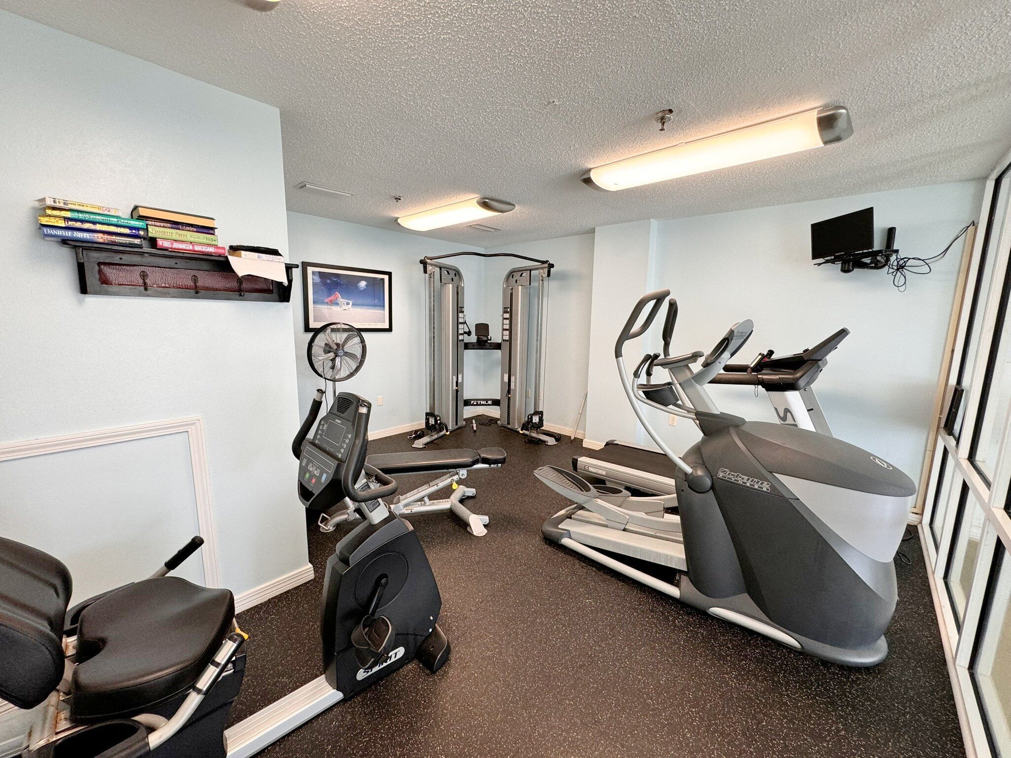 A gym with cardio equipment, weight machines, and a wall-mounted TV.