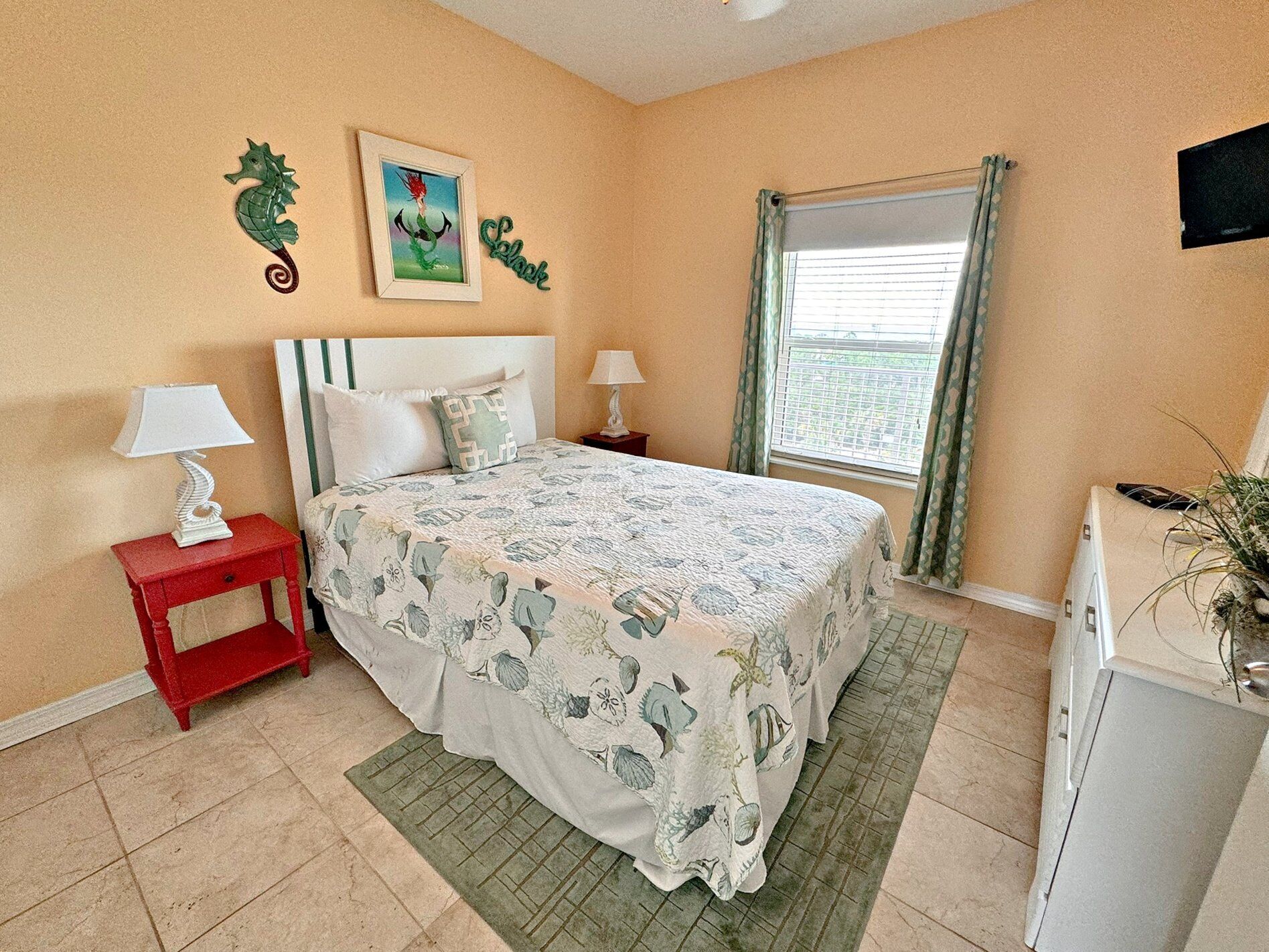 Une chambre à coucher comprenant un lit, deux tables de chevet, une commode, une coiffeuse, une fenêtre avec des rideaux et des éléments de décoration murale.
