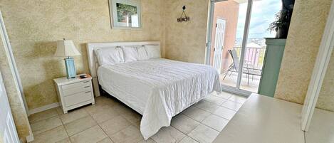 A bedroom with a bed, a nightstand, a ceiling fan, and a view of the outside balcony.