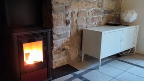 A stone wall, a fireplace with a visible fire, and a white cabinet. - PENTY CHEZ GERMAINE, 5 MINUTES FROM LE FRET PORT (Crozon)
