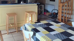 A cozy kitchen with wooden beams, a dining area with a quilted table, and a spiral staircase. - PENTY CHEZ GERMAINE, 5 MINUTES FROM LE FRET PORT (Crozon)