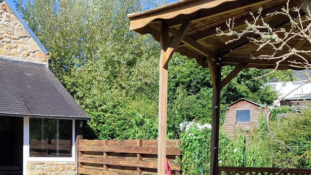 A backyard with a barbecue grill, wooden pergola, and a stone house in the background. - PENTY CHEZ GERMAINE, 5 MINUTES FROM LE FRET PORT (Crozon)