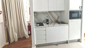 Une cuisine de taille réduite avec des meubles blancs, un four à micro-ondes encastré et un évier.