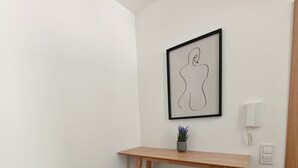 Un petit bureau en bois, avec une œuvre d’art abstraite encadrée accrochée au-dessus, une plante en pot posée sur le bureau et deux tabourets en bois.