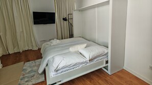Une chambre à coucher avec un lit, un téléviseur fixé au mur et une armoire.