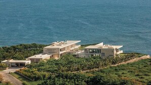 Uma propriedade costeira moderna com vários edifícios, vista para o mar e vegetação exuberante.