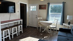 A compact living space with a dining area, a sofa, a TV mounted on the wall, and a ceiling fan. - This cozy house has been completely remodeled inside and features three bedrooms. (Helena)