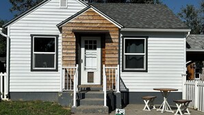 A two-story house with a front porch, a small table and benches, and a sign requesting dog owners to clean up after their pets. - This cozy house has been completely remodeled inside and features three bedrooms. (Helena)