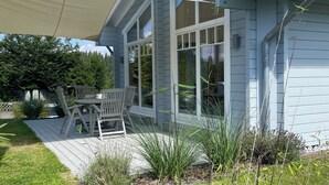 Une maison moderne dotée d’un patio couvert, d’un coin repas et offrant une vue sur la verdure environnante.