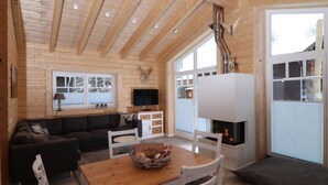 L’intérieur d’un chalet confortable, avec un plafond en bois, une cheminée, un coin repas et une grande fenêtre.