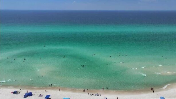 A beach with clear turquoise water, people swimming, and beach umbrellas.