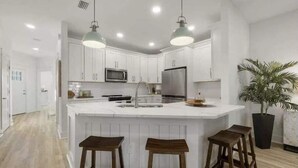 A modern kitchen with white cabinetry, a central island with stools, stainless steel appliances, and pendant lighting.