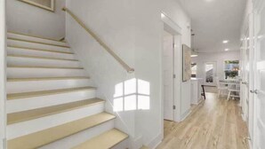 A staircase with a handrail, a dining area with a table and chairs, and a kitchen area with cabinets and a window.