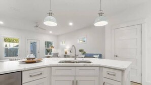 A modern kitchen with white cabinetry, a central island, pendant lighting, and a view of the backyard.