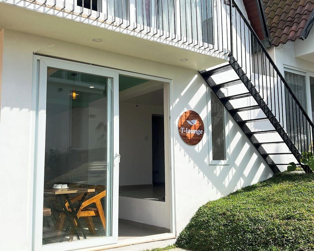 A modern building with a glass door entrance, a wooden sign reading "T-lounge," and a black staircase leading to an upper floor.