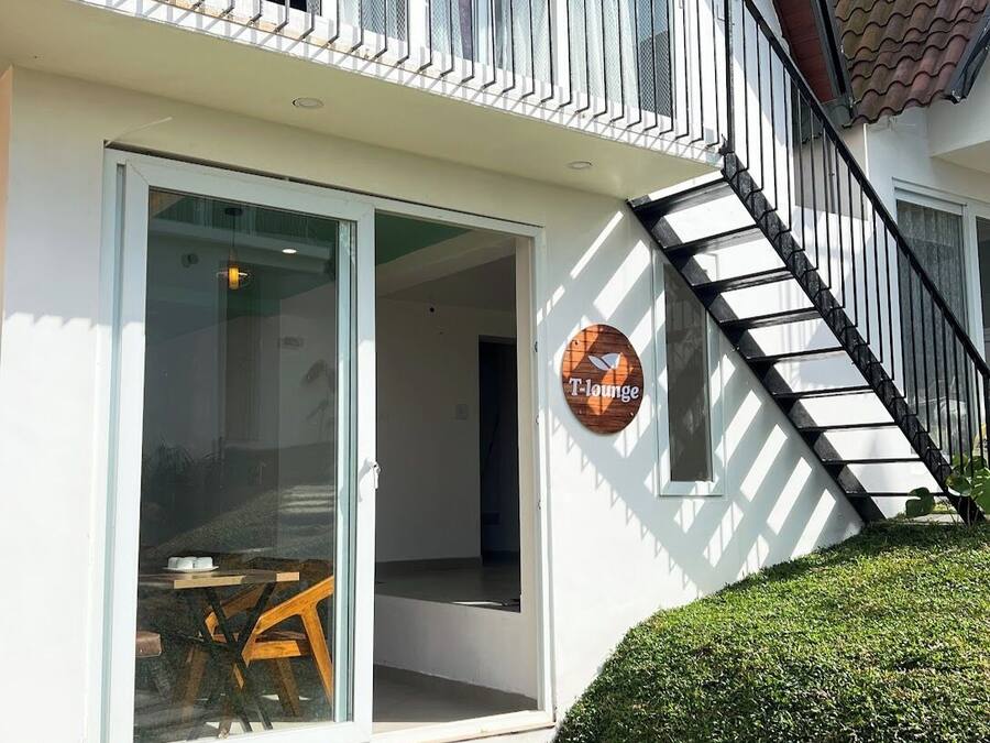 A modern building with a glass door entrance, a wooden sign reading "T-lounge," and a black staircase leading to an upper floor.