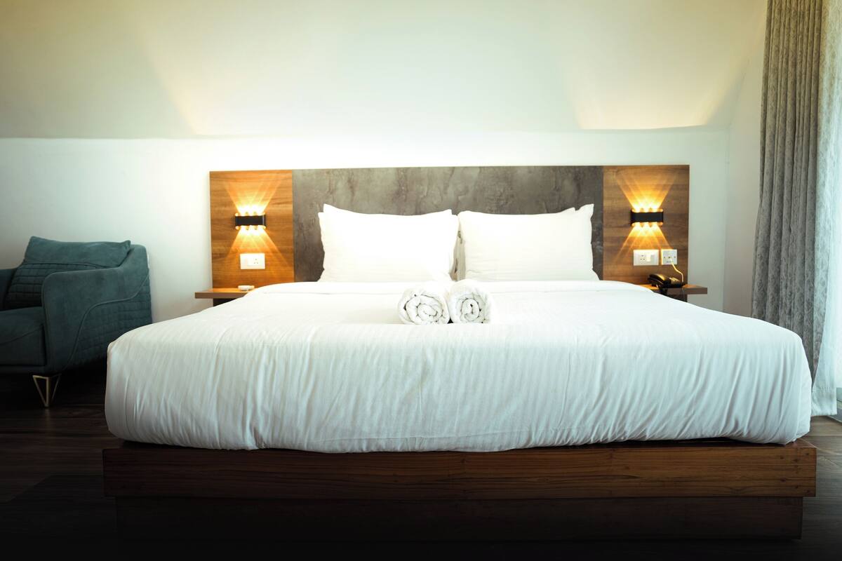A large bed with a wooden headboard, two bedside tables with wall-mounted lamps, and a green armchair.