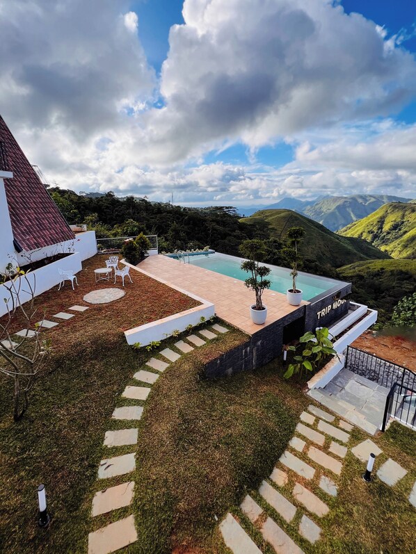 A pool area with a view of mountains, surrounded by a garden with stepping stones and potted plants. - TRIP MOUNT (Peermade)
