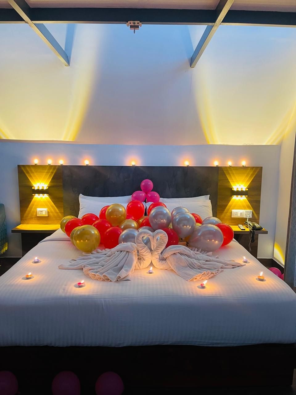 A hotel room with a large bed, decorative balloons, and wall-mounted lamps.