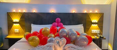 A hotel room with a large bed, decorative balloons, and wall-mounted lamps.