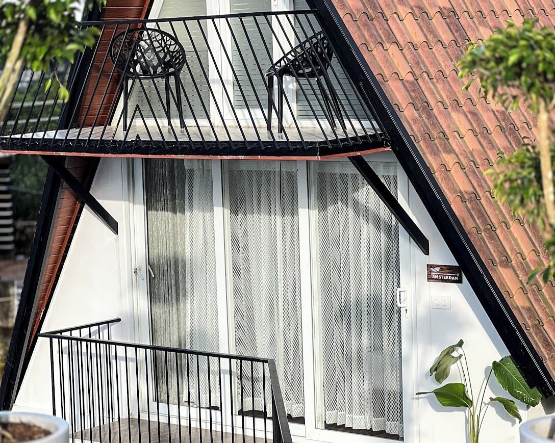 Una casa moderna con techo inclinado, un balcón con barandillas negras y un letrero que dice 'AMSTERDAM'.