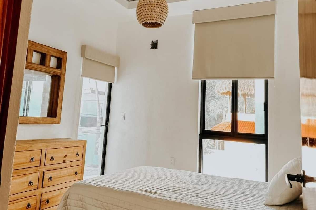 Quarto com cama, cómoda de madeira e teto com vigas aparentes.