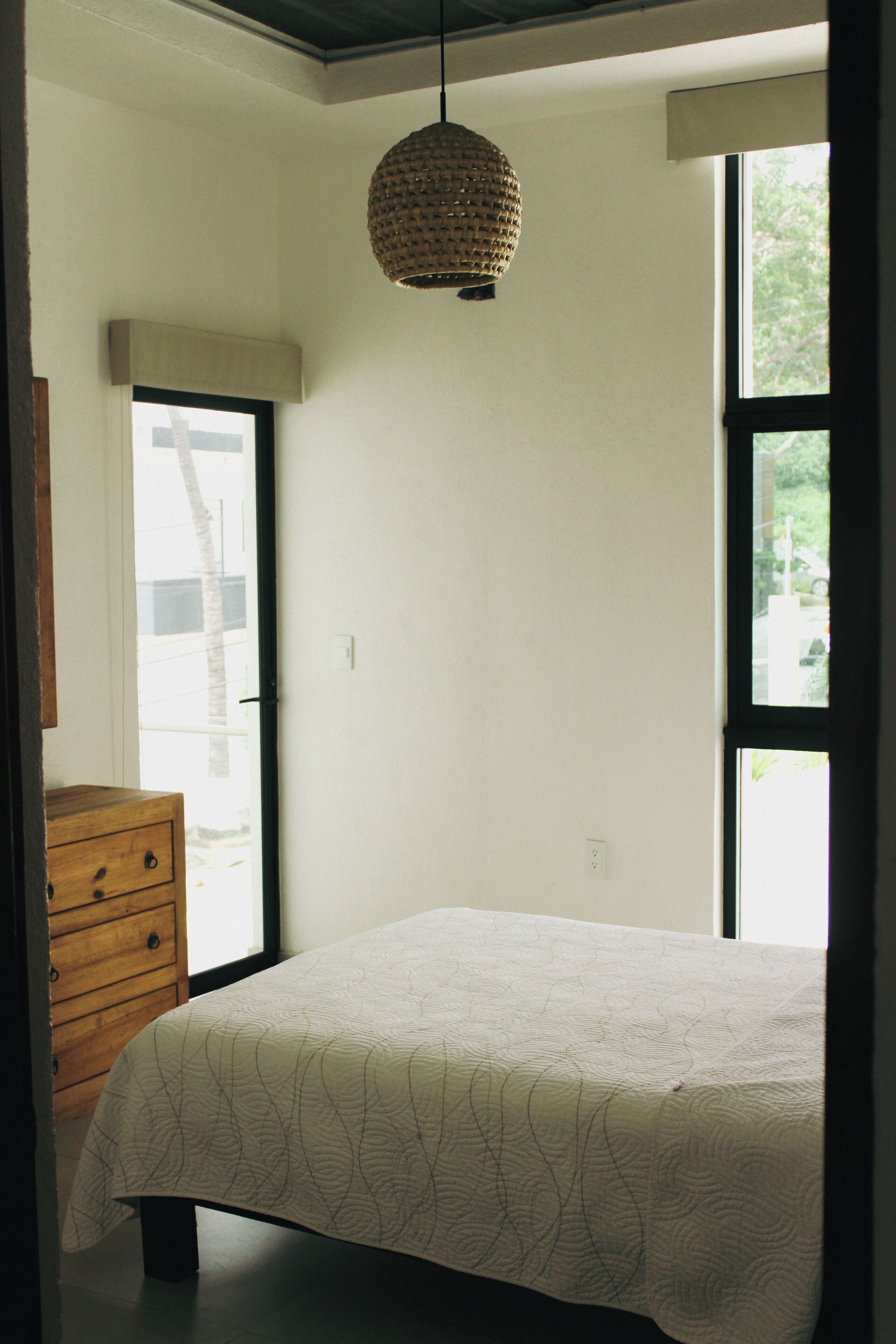 Ein Schlafzimmer mit Bett, Schminktisch, Pendelleuchte und großen Fenstern.