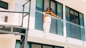 Una persona parada en un balcón de un edificio moderno con ventanas amplias y barandilla de vidrio.