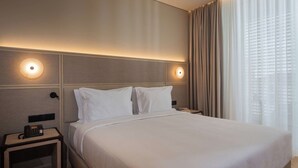 Ein Hotelzimmer mit einem großen Bett, zwei Nachttischen, einem Telefon und einem Fenster mit Vorhängen.