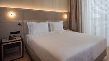 Quarto de hotel com uma cama grande, duas mesas de cabeceira, um telefone e uma janela com cortinas.