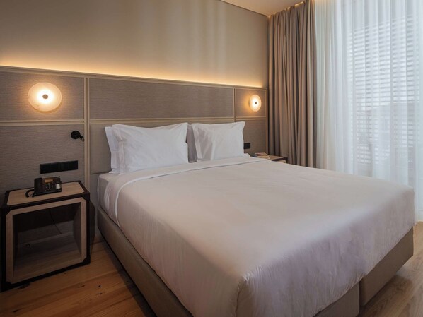 Ein Hotelzimmer mit einem großen Bett, zwei Nachttischen, einem Telefon und einem Fenster mit Vorhängen.