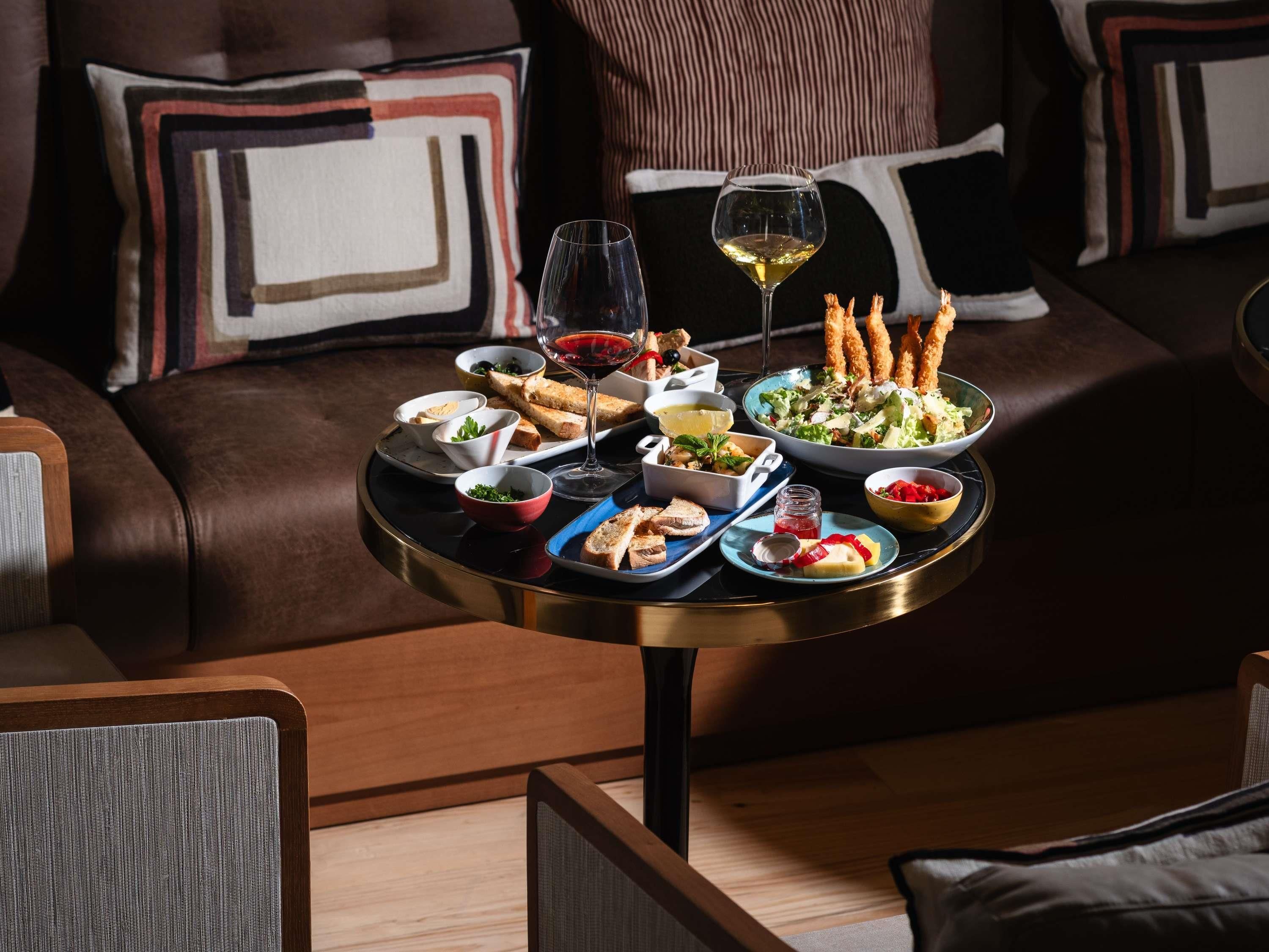 Una mesa de comedor con diversos platos y bebidas, sobre un sofá de cuero con cojines estampados.