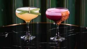 Zwei Cocktails auf einer spiegelnden Fläche vor einem grün gestreiften Hintergrund.