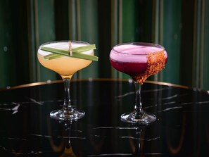 Zwei Cocktails auf einer spiegelnden Fläche vor einem grün gestreiften Hintergrund.