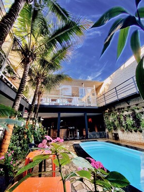 A pool area with palm trees, a covered seating area, and a wall of hanging plants. - Hostel Gravatá (Piracicaba)