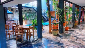 An indoor patio with a pool, wooden tables and chairs, potted plants, and a tiled floor. - Hostel Gravatá (Piracicaba)