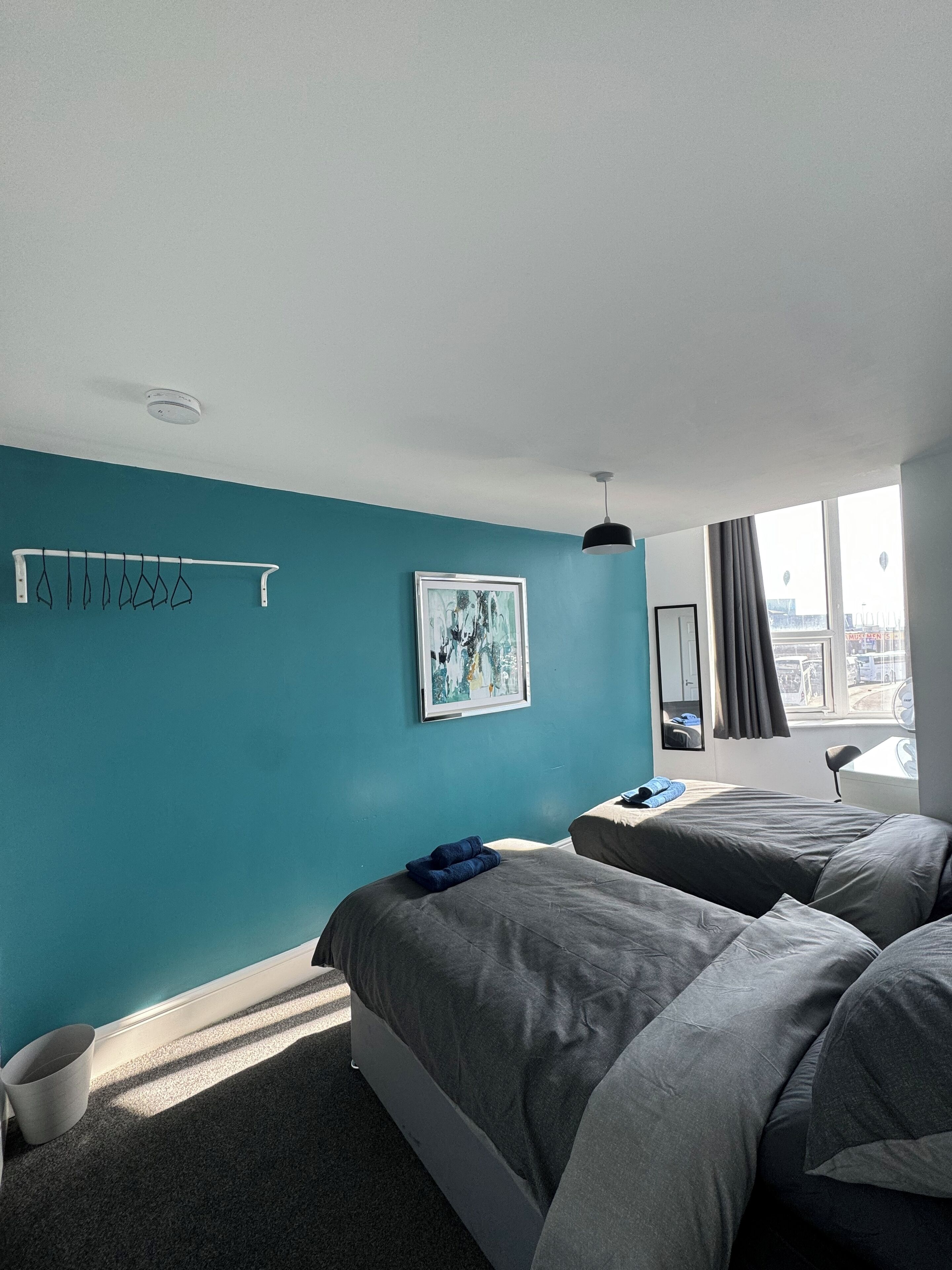 Moderni hotellihuone, jossa on turkoosinsiniset seinät, suuri sänky, pieni työpöytä ja ikkuna, josta avautuu näkymä kaupunkiin.