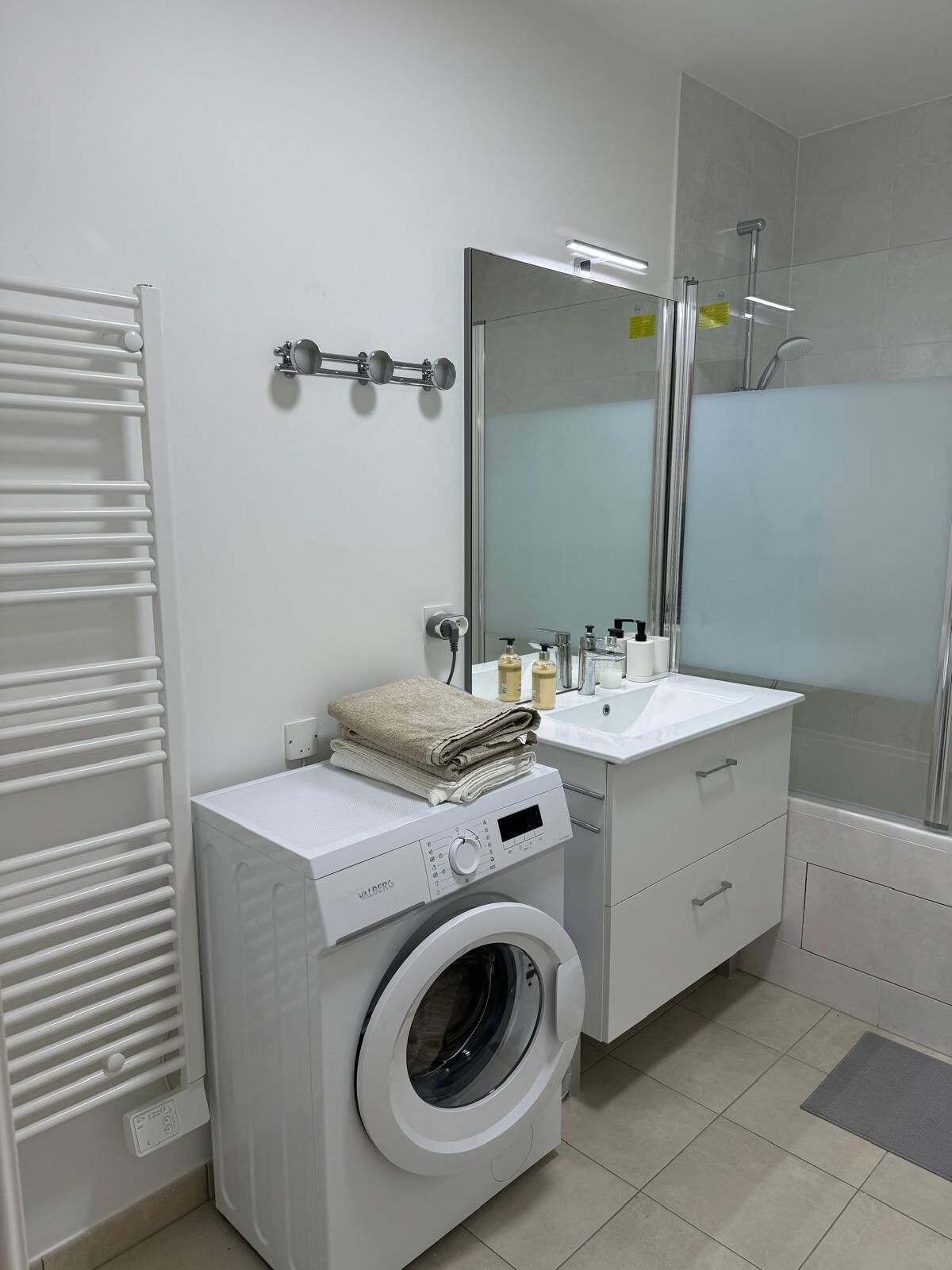 Un bagno moderno con lavatrice integrata, un lavandino, uno specchio e una doccia.