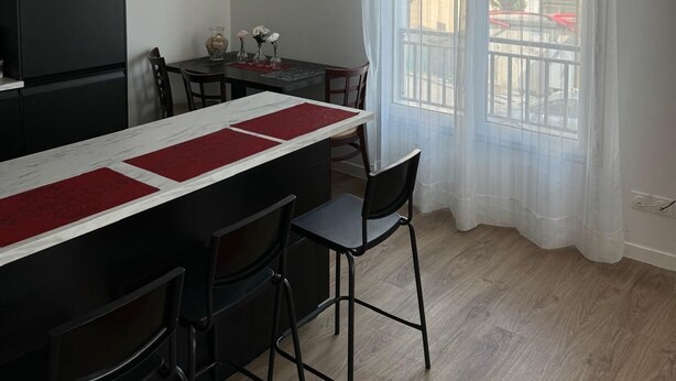 Una cocina compacta con comedor, que cuenta con una encimera negra, salpicadero de mármol blanco y una mesa de comedor con individuales rojos.
