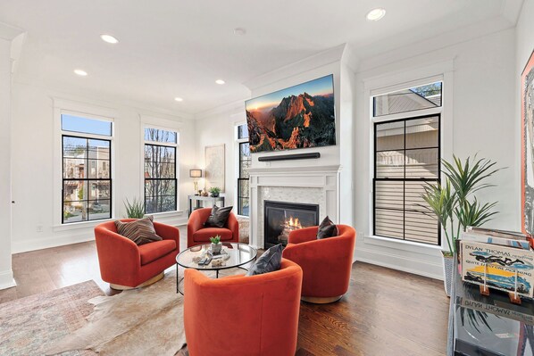 A modern living room with a fireplace, large windows, and red armchairs. - Spacious 5-bedroom house w/Elevator and Game room!! (Nashville)