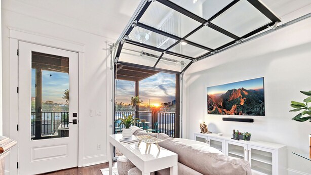 Un salon moderne doté d’un plafond en verre, d’un grand téléviseur et d’un balcon offrant une vue sur le coucher du soleil.